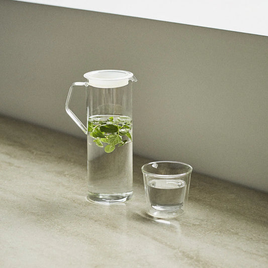 Clear glass pitcher and cup with water and mint leaves on a neutral background